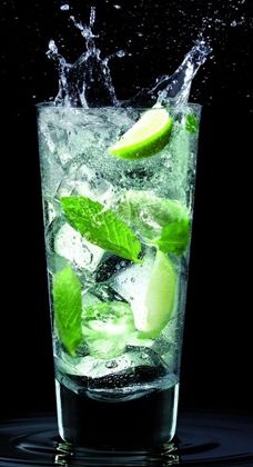 a glass filled with ice and limes on top of a black table next to water