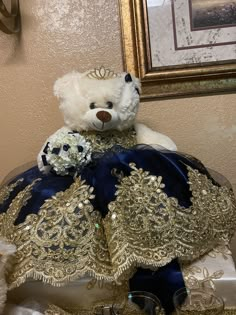 a white teddy bear wearing a blue and gold dress sitting on top of a table