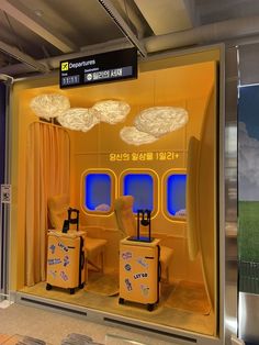 two suitcases sitting in front of a window with yellow curtains and clouds above them