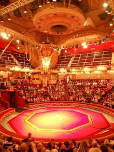 an auditorium filled with people and lots of red carpeted seats in front of the stage