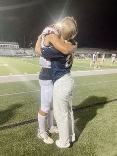 two people hugging each other on a field at night time with the stadium lights in the background