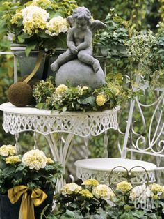 there are many potted plants and flowers on the table in the garden with an angel statue