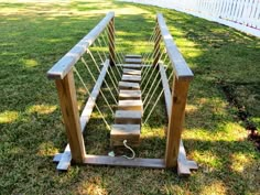 a set of stairs made out of wood and rope on the grass in front of a white picket fence