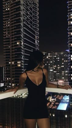 a woman standing on top of a balcony next to tall buildings in the city at night