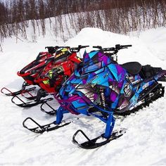 three colorful snowmobiles parked in the snow