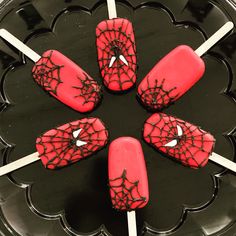 four red cake pops with spider web designs on them sitting on a black plate in the shape of a flower