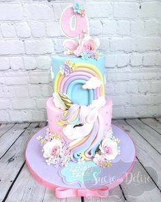 a cake decorated with an unicorn and flowers on top of a wooden table next to a brick wall