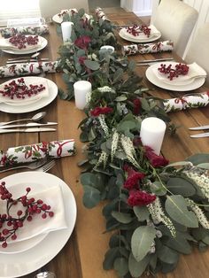 the table is set with white plates, silverware and greenery on it's edges