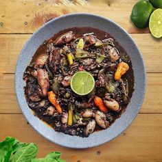 a bowl filled with meat and vegetables on top of a wooden table next to limes