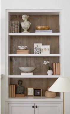 a white bookcase with books and other items on it's shelves next to a lamp