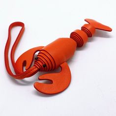 an orange plastic lobster on a white surface with a red strap around it's neck