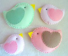 three felt birds sitting next to each other on a white table cloth covered surface with yellow, pink, and green accents