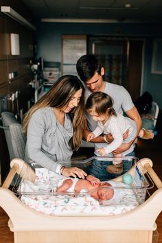 a man, woman and baby are sitting in a crib looking at their newborn