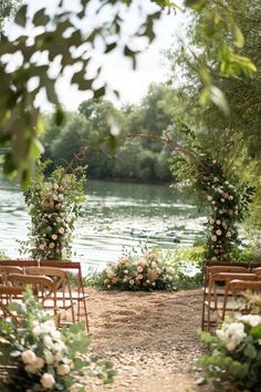 an outdoor ceremony set up with chairs and flowers on the ground next to water, surrounded by greenery