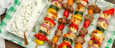 several skewers of meat and veggies on a tray with dip in the middle