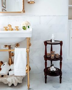 An antique stained wood three-tier bathroom shelf stands next to a vintage white console sink with gold metal legs. The sink is fitted against a white and gray marble tile half wall. Complement the wainscoting with a marble hexagon tile floor...   Image: nicholnaranjo