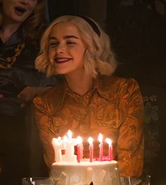 a woman sitting in front of a cake with lit candles