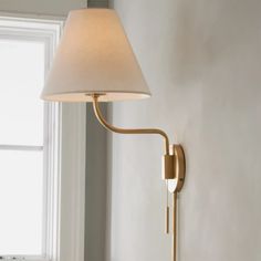 a wall lamp with a white shade on it in front of a window, next to a bed