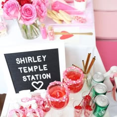 a table topped with lots of pink flowers and cups filled with liquid next to a sign