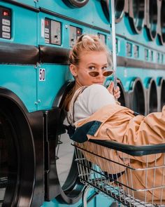 a woman sitting in a shopping cart next to a blue bus