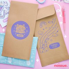 two brown envelopes sitting next to each other on top of a pink table with markers and pens