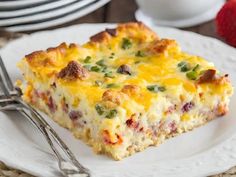 a slice of quiche on a white plate with a fork and strawberries in the background