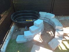 a black tub sitting in the middle of a yard next to some rocks and grass