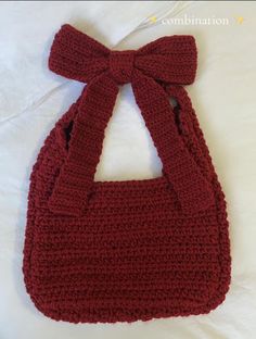 a red crocheted purse with a bow on the front and side, sitting on a bed