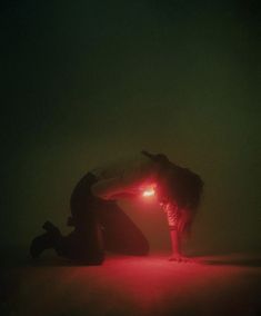 a man kneeling down with a red light on his face in the middle of a dark room