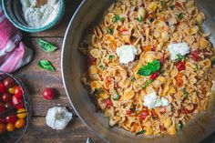 a pan filled with pasta and vegetables on top of a wooden table next to other dishes