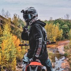 a man riding on the back of a motorcycle down a dirt road next to a forest