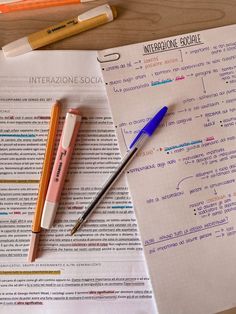 two pens sitting on top of a paper next to some writing utensils and pencils