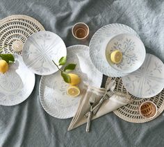 four plates with lemons on them sitting on a bed next to cups and utensils