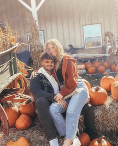 a man and woman sitting on hay bales with pumpkins in the back ground