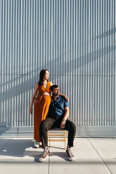 a man and woman sitting on a bench in front of a metal wall with shadows