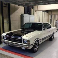 an old white car parked in a garage next to a man walking by the door