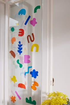 the window is decorated with colorful paper cutouts and flowers in front of it, as well as a vase full of yellow flowers