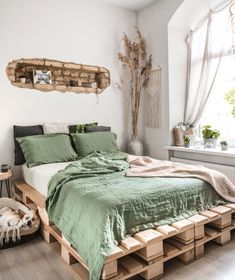 a bed made out of wooden pallets with green sheets and blankets on top of it