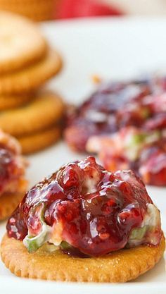 crackers with jelly and cheese on them sitting on a white plate next to cookies