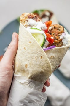 a hand holding a pita filled with meat and veggies