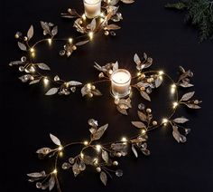 two candles are sitting next to each other on a table with leaves and lights around them