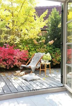 a chair and table on a wooden deck in front of a glass door that leads to a garden