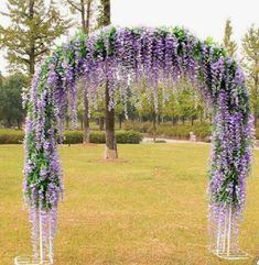 an outdoor wedding ceremony with purple and green flowers on the arch, in front of a tree