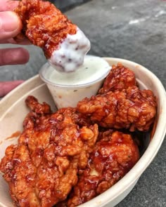 a person dipping something into a bowl with chicken wings on it and sauce in the middle