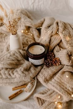 a white plate topped with a candle next to a blanket and pine cones on top of it