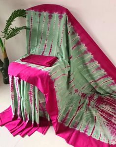 a pink and green tie - dyed table cloth with matching napkins sits on a white surface next to a potted plant