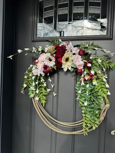 a wreath is hanging on the front door with flowers and greenery around it,