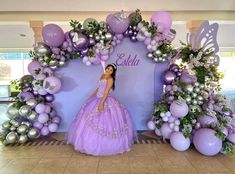 a woman in a purple dress is standing next to balloons and garlands on the wall