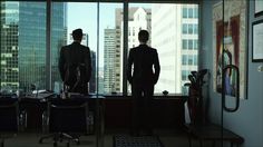 two men standing in an office looking out the window at cityscape and skyscrapers