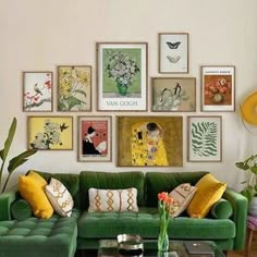 a green couch sitting in front of a wall filled with pictures and paintings on it